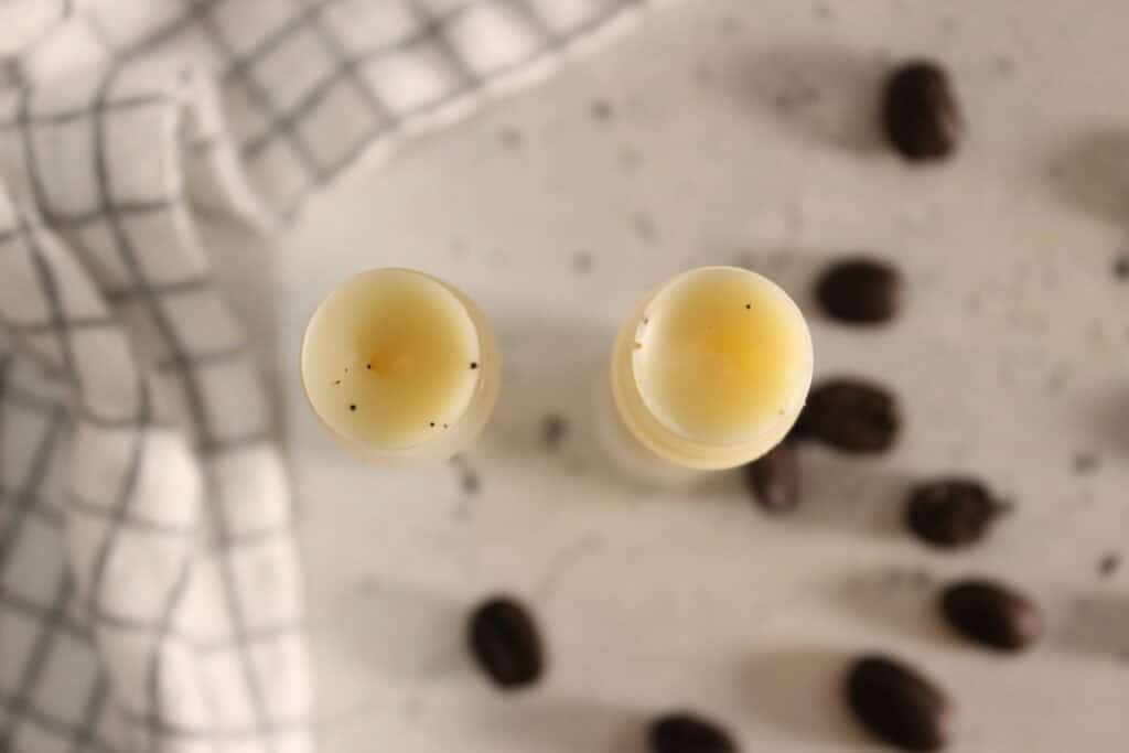 Top view of two open tubes of DIY coffee lip balm, with coffee beans scattered around.