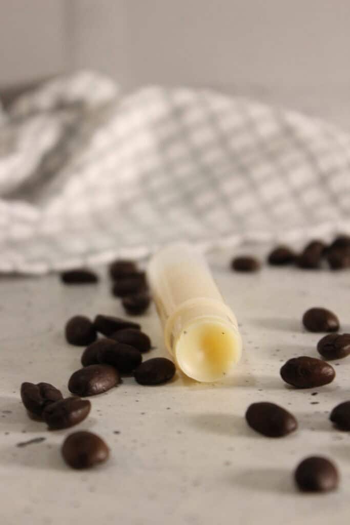 coffee lip balm arranged flat with coffee beans scattered around on a light surface, styled with a checkered cloth.