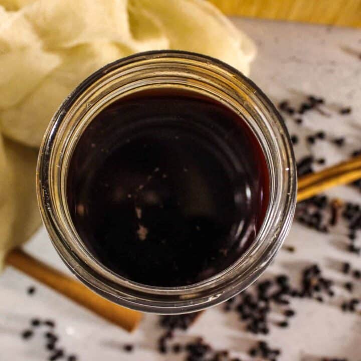 close up view of Jar of homemade elderberry syrup with cinnamon sticks.