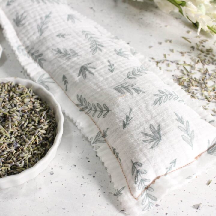 Lavender sachet with leaf-print fabric, dried lavender in a bowl, loose lavender buds, and white flowers on a light surface.