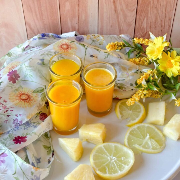 Pineapple ginger wellness shots served in small glasses with fresh lemon slices and pineapple pieces.