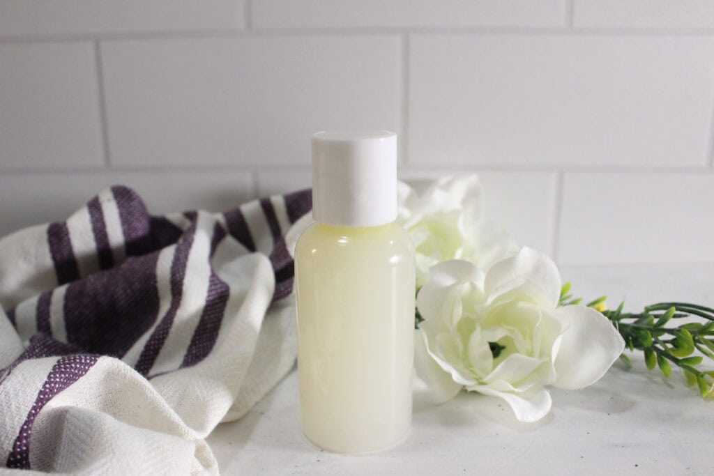 Herbal micellar water in a bottle, styled with a white flower and a cloth in the background.