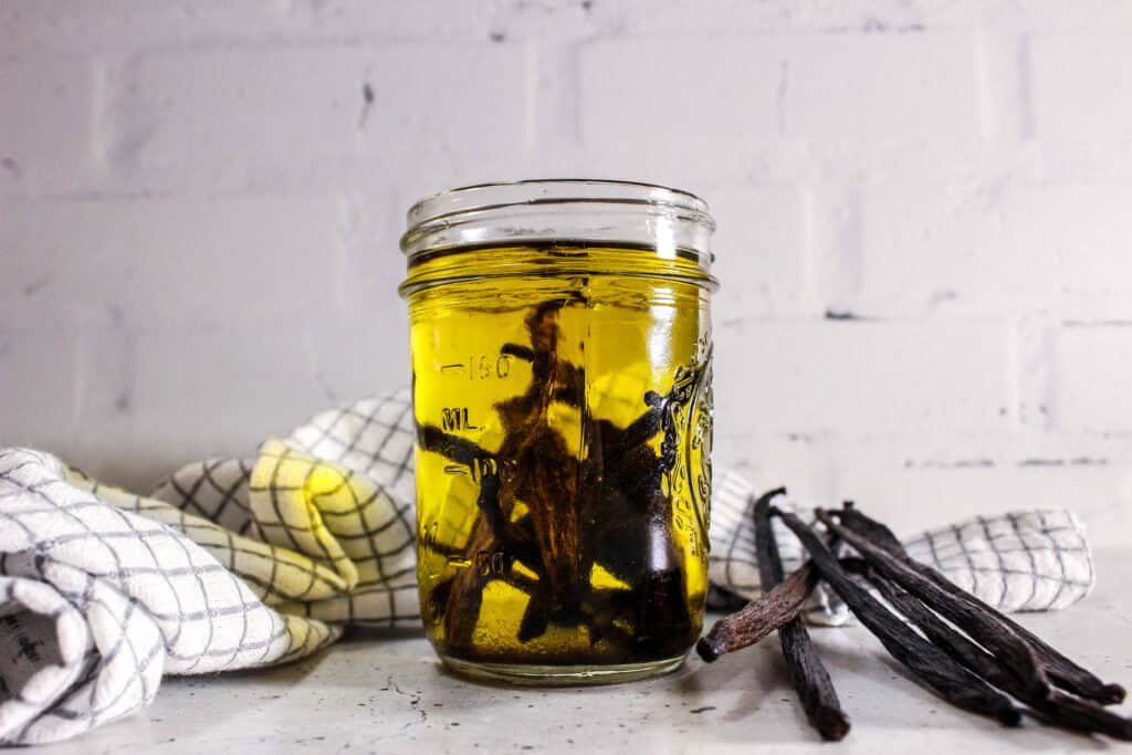 Vanilla beans steeping in golden oil inside a glass jar.