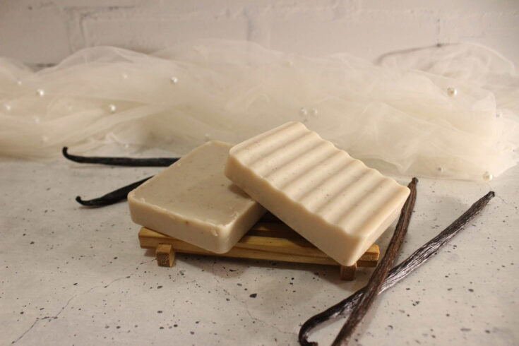 Two vanilla soaps stacked on a wooden soap tray, with vanilla beans beside them.