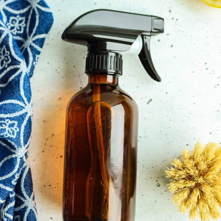 Amber cleaning spray bottle with trigger top beside half lemon and wooden scrub brush.