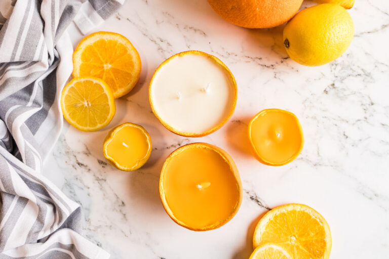 Bright yellow citrus peel candles with fresh lemons and oranges on marble surface.