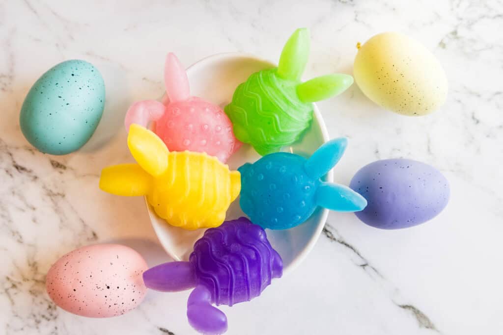 Colorful Easter bunny-shaped soaps with pastel eggs on marble background.