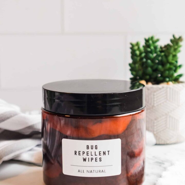 Amber glass jar of homemade bug repellent wipes with black lid and white label on marble surface