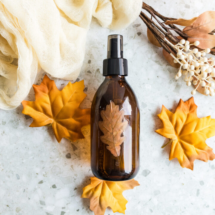 Amber spray bottle surrounded by autumn leaves, cinnamon sticks, and dried botanicals.