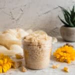 Homemade frankincense sugar scrub in glass jar surrounded by yellow flowers and natural ingredients
