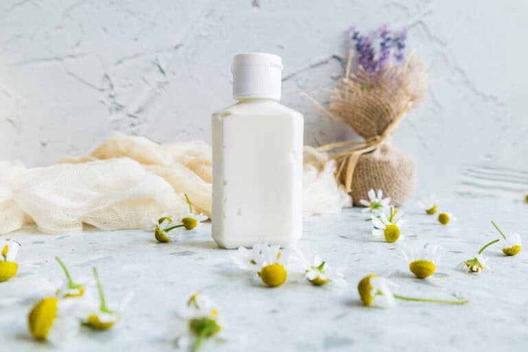 White lotion bottle placed on a marble surface with chamomile flowers beside it.