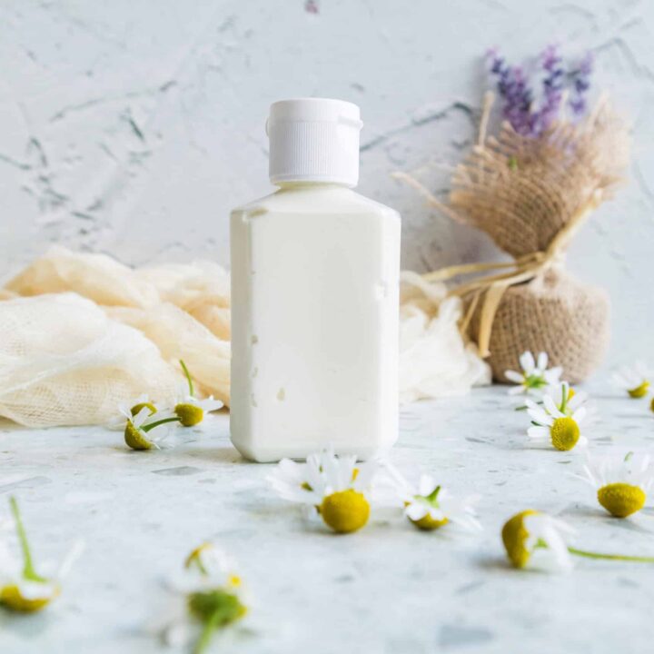 White lotion bottle placed on a marble surface with chamomile flowers beside it.