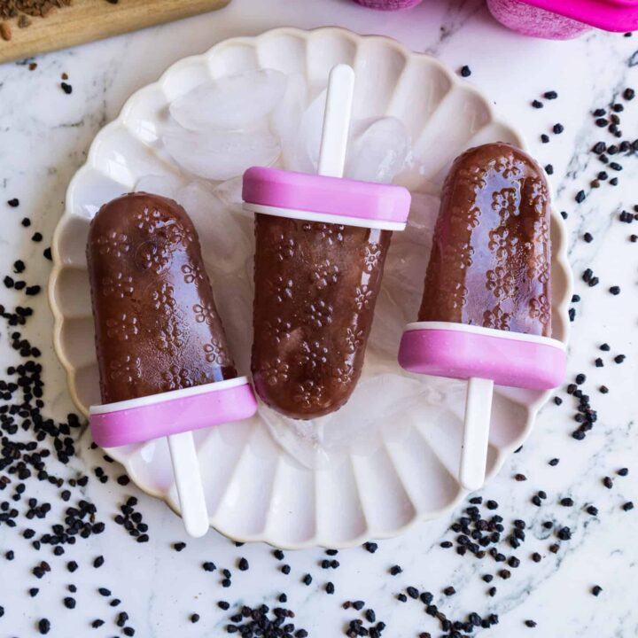 Three elderberry popsicles arranged on a white plate.