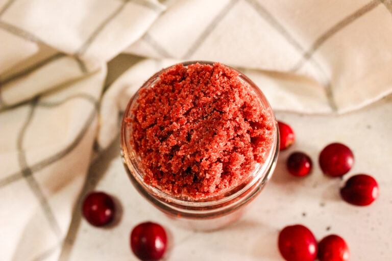Top view of a jar containing red cranberry sugar scrub with cranberries placed beside it.