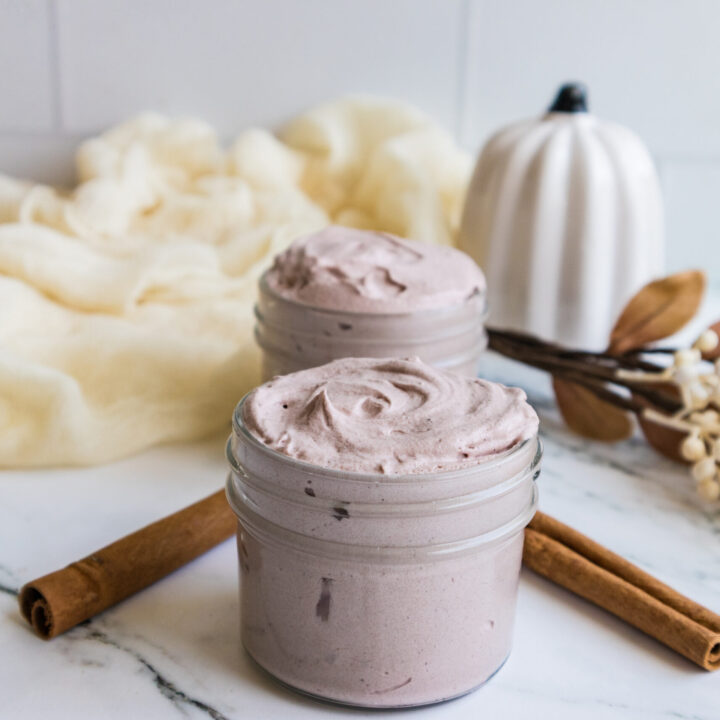 Two open jars of Whipped Tallow Balm with cinnamon sticks and autumn leaves on a marble surface.