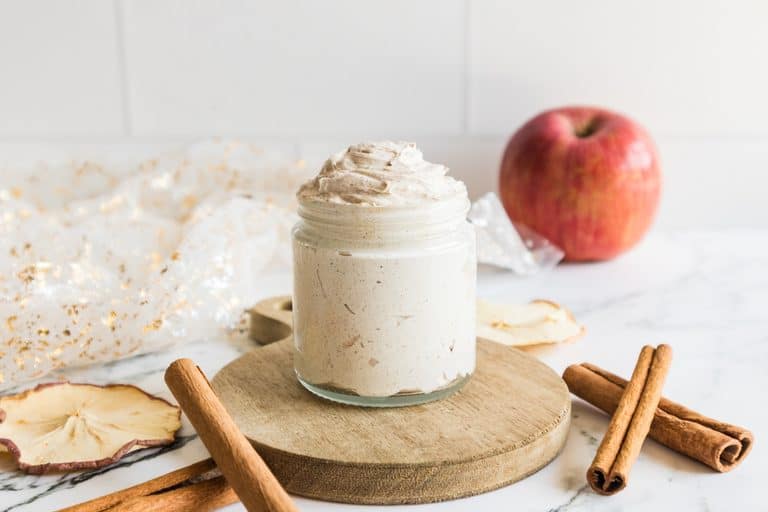 Glass jar filled with creamy whipped butter placed with cinnamon sticks and apple slices.