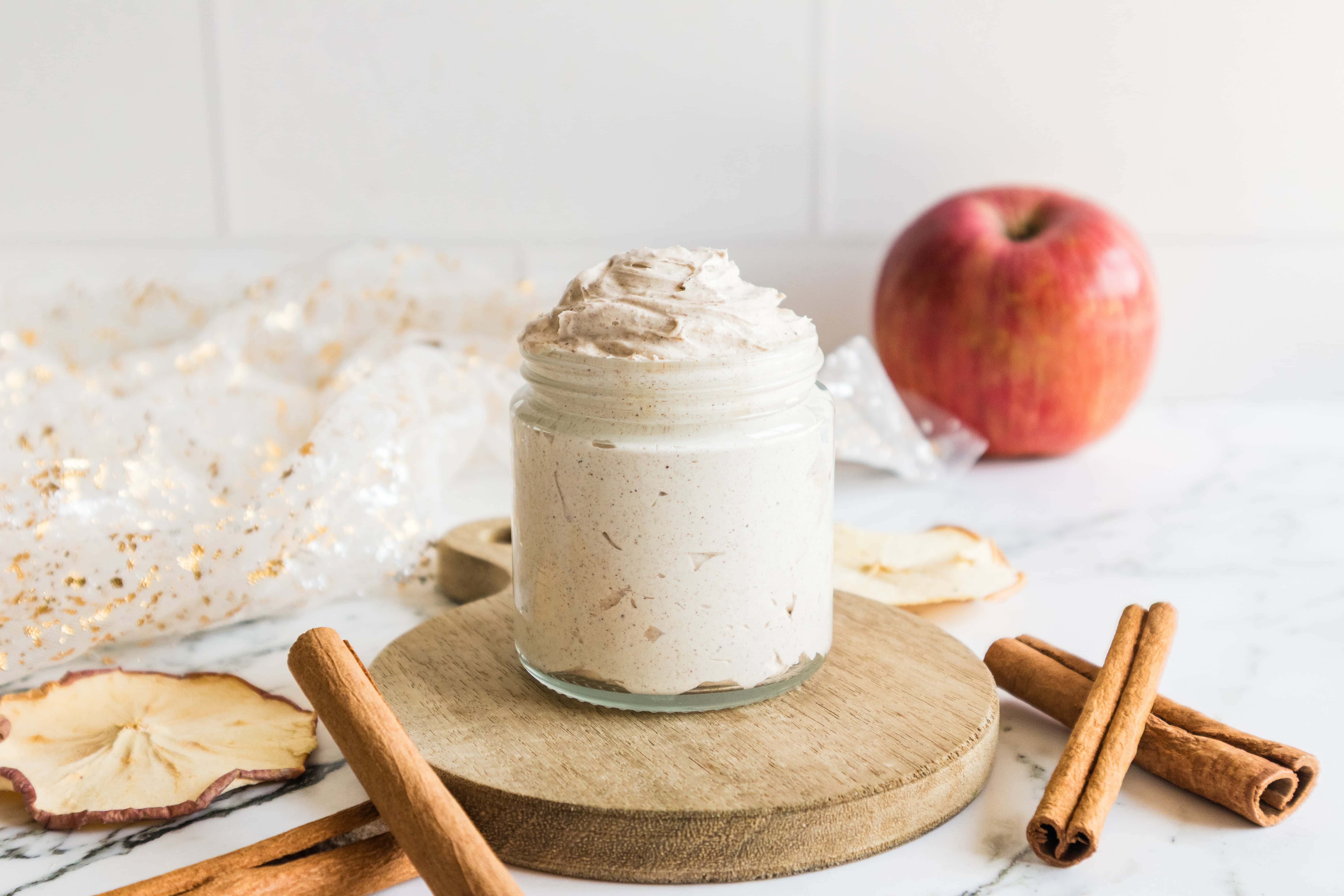 Glass jar filled with creamy whipped butter placed with cinnamon sticks and apple slices.