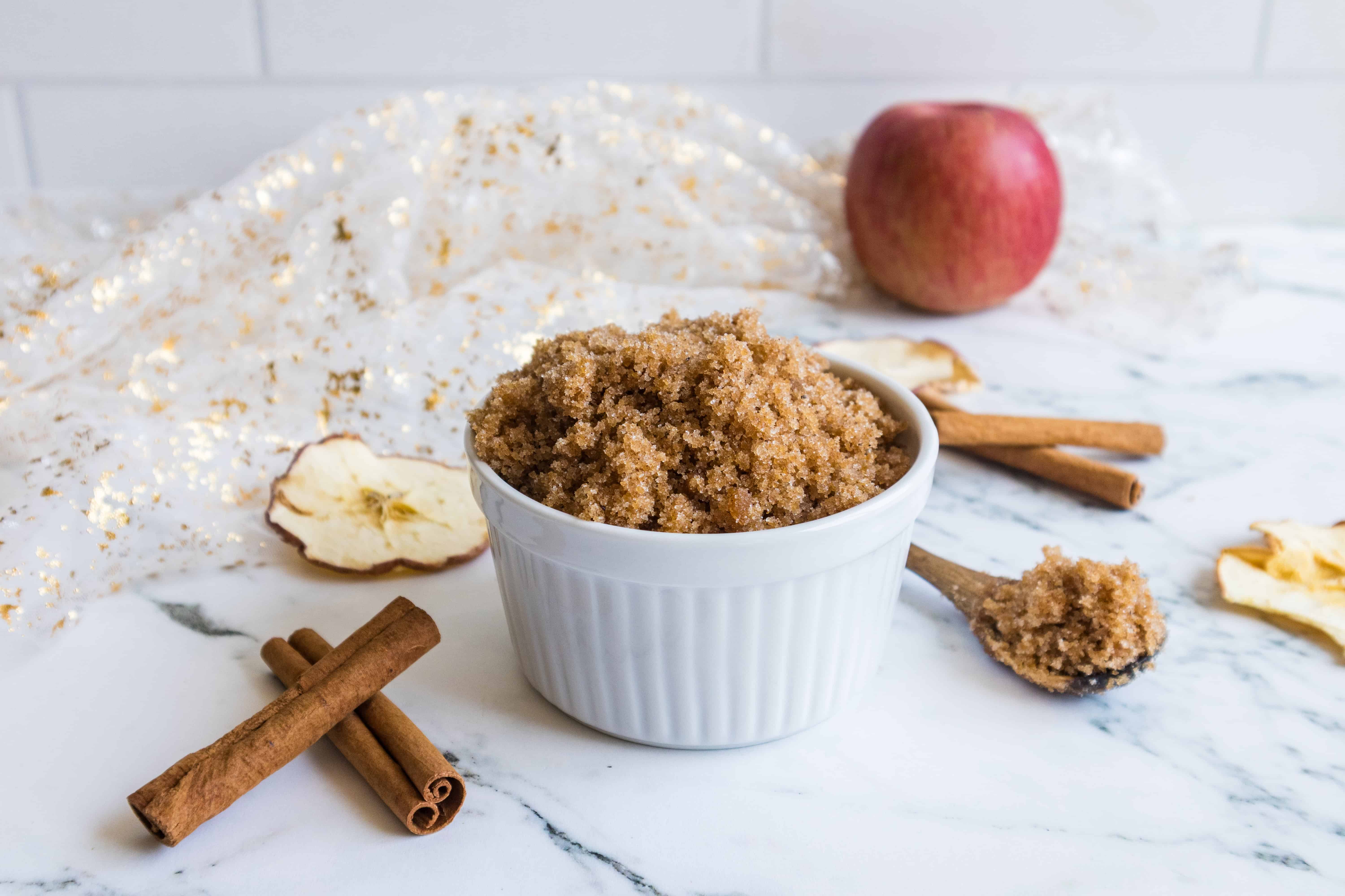 Close-up of homemade sugar scrub in a white ramekin with apple and cinnamon accents.